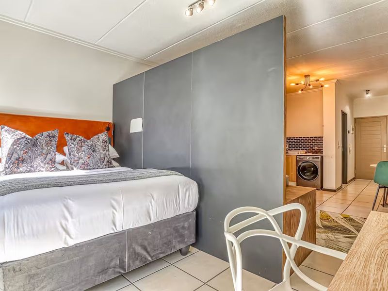 Open-plan apartment layout featuring a bedroom area separated by a partition wall from the kitchen and laundry space with tiled flooring throughout.