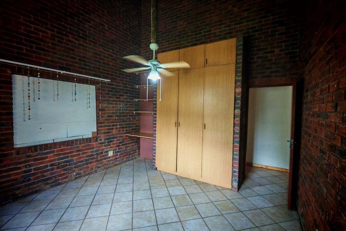 A bedroom featuring exposed brick walls, built-in wooden cabinetry, tiled flooring, and a ceiling fan.