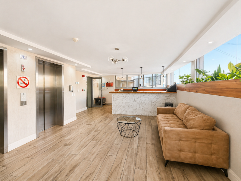 Modern apartment building lobby featuring a reception desk with marble-look tiling, wood-look floor tiles, and a stainless steel elevator.