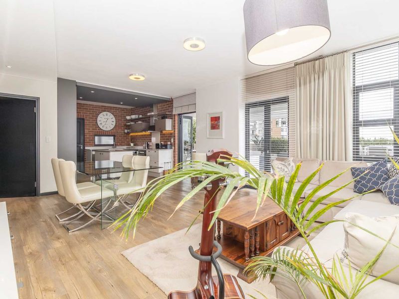 Spacious open-plan living and dining area featuring modern laminate flooring, an exposed brick kitchen wall, and seamless access to the outdoor patio.