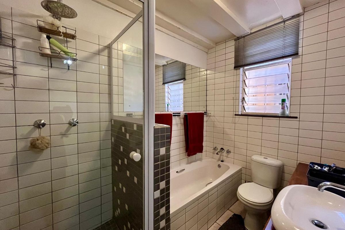 A functional bathroom featuring a separate shower enclosure, a built-in bathtub, a toilet, and a vanity basin with tiled walls.
