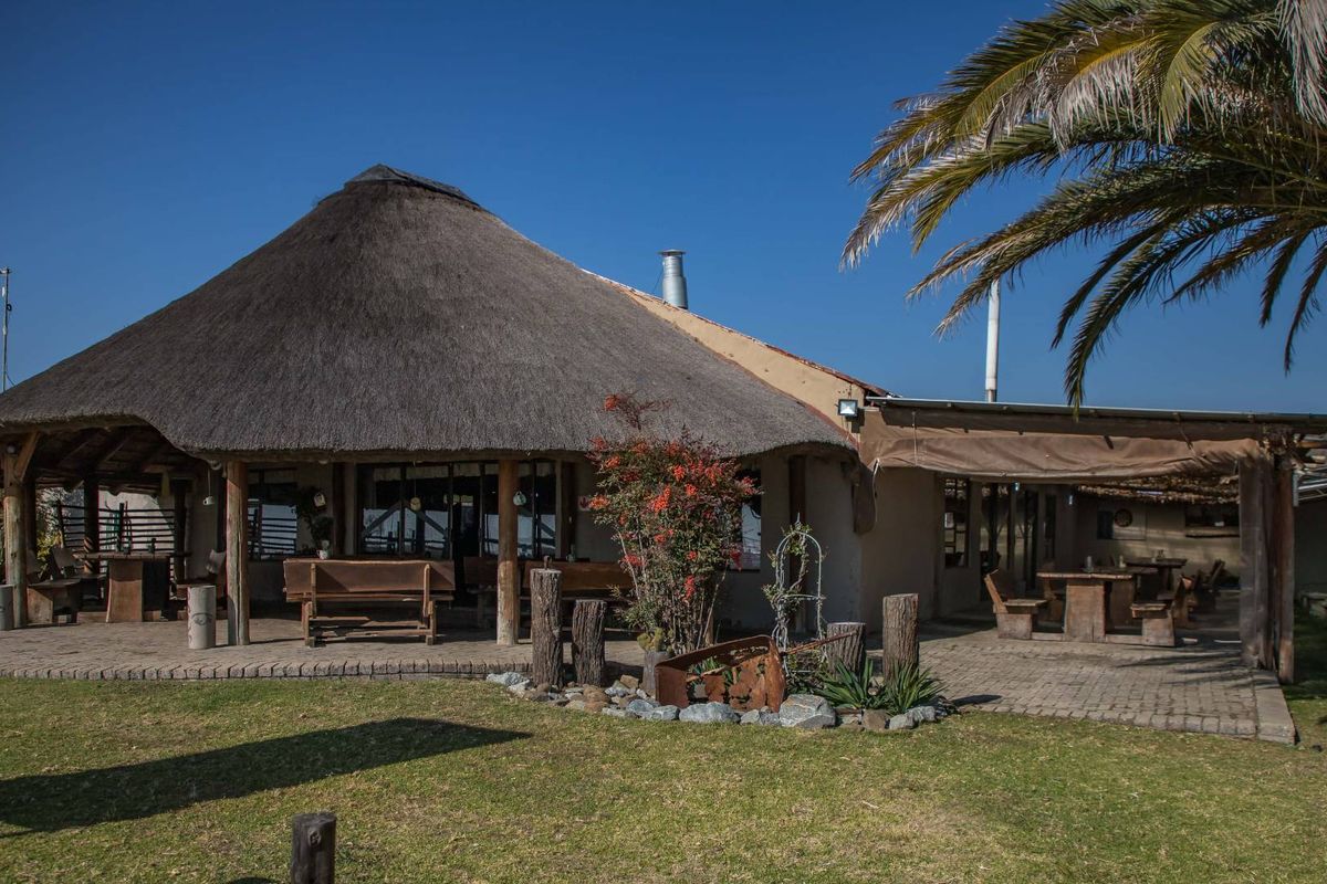 A rustic farm-style dwelling featuring a traditional thatched roof, expansive covered patio area, and established garden surroundings.