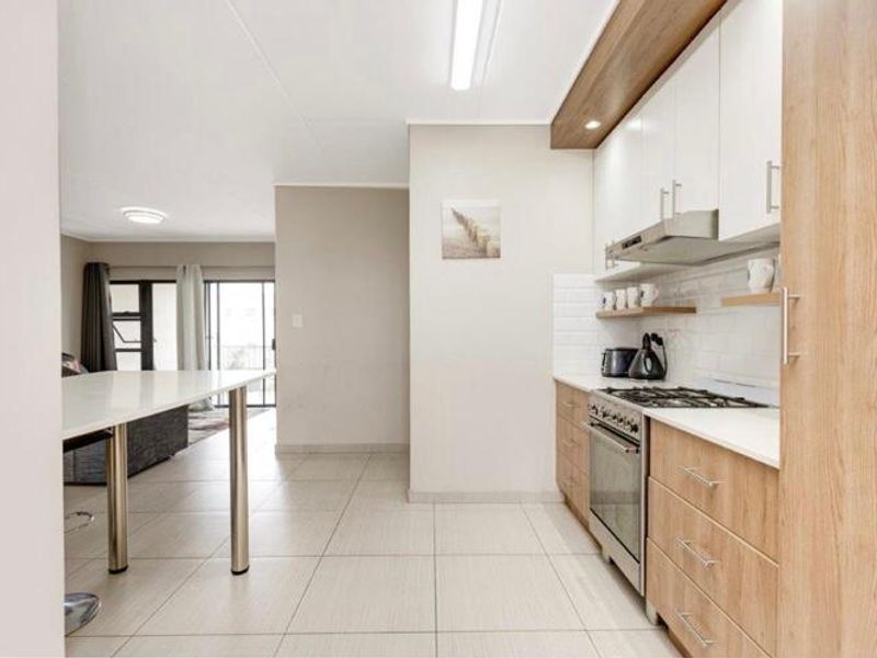 Modern open-plan kitchen featuring light wood cabinetry, stone countertops, gas hob, and integrated appliances, flowing into a bright living area.