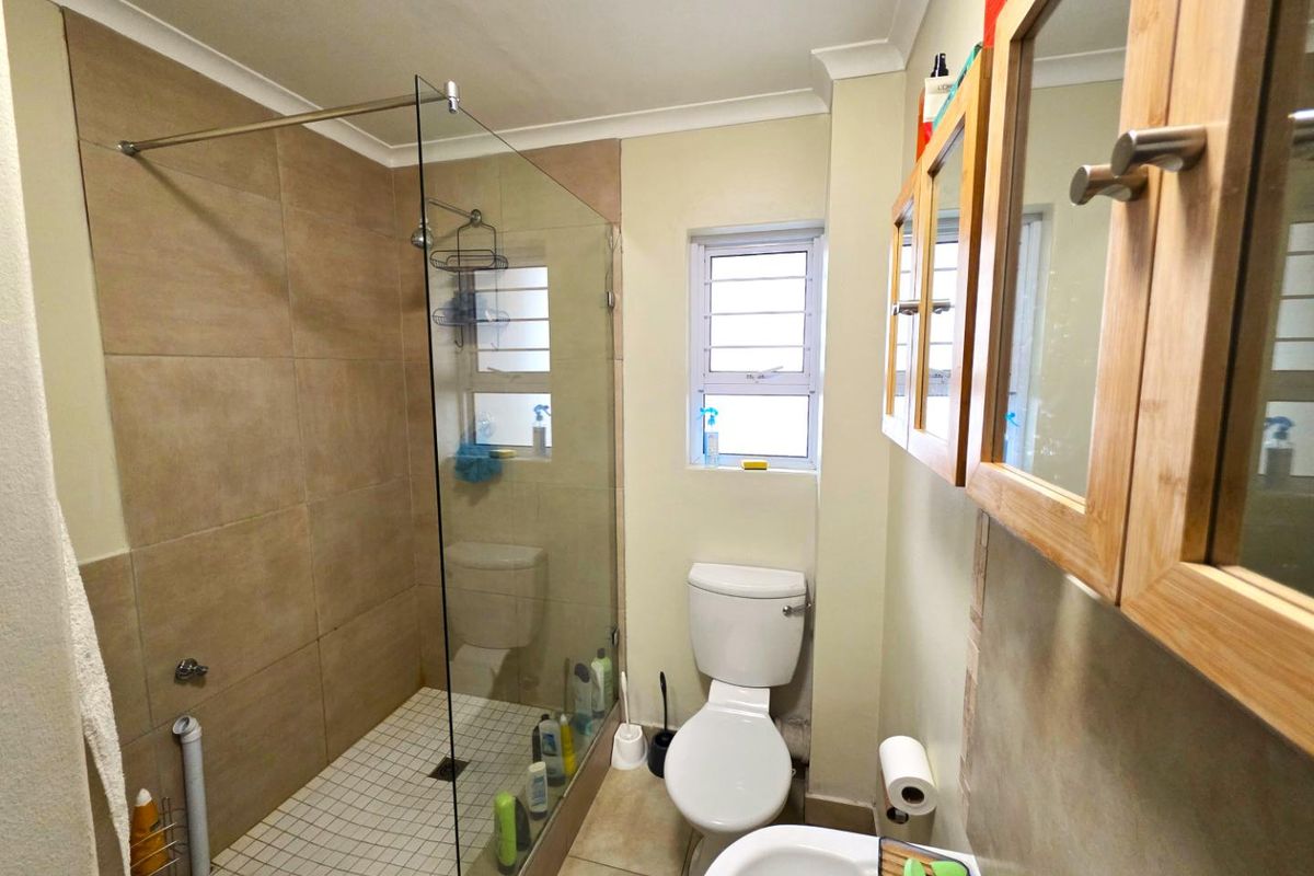 A functional bathroom featuring a walk-in glass shower enclosure, tiled flooring, a wall-mounted toilet, and wooden cabinetry with integrated mirrors.