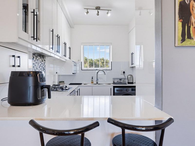 Modern kitchen featuring white high-gloss cabinetry, quartz countertops, a gas hob, and a mosaic tile backsplash with a functional breakfast bar area.