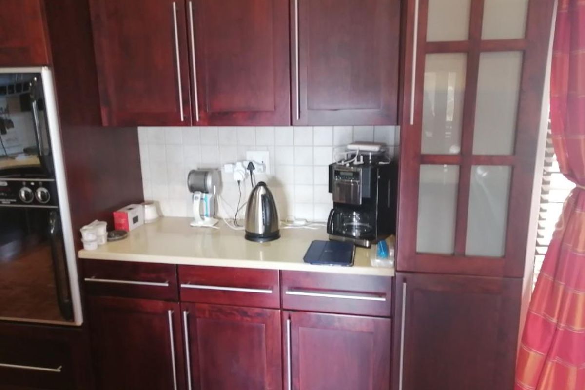 A kitchen area featuring dark wood cabinetry, a light-toned countertop, and a tiled backsplash with integrated oven and glass-paneled cabinet storage.