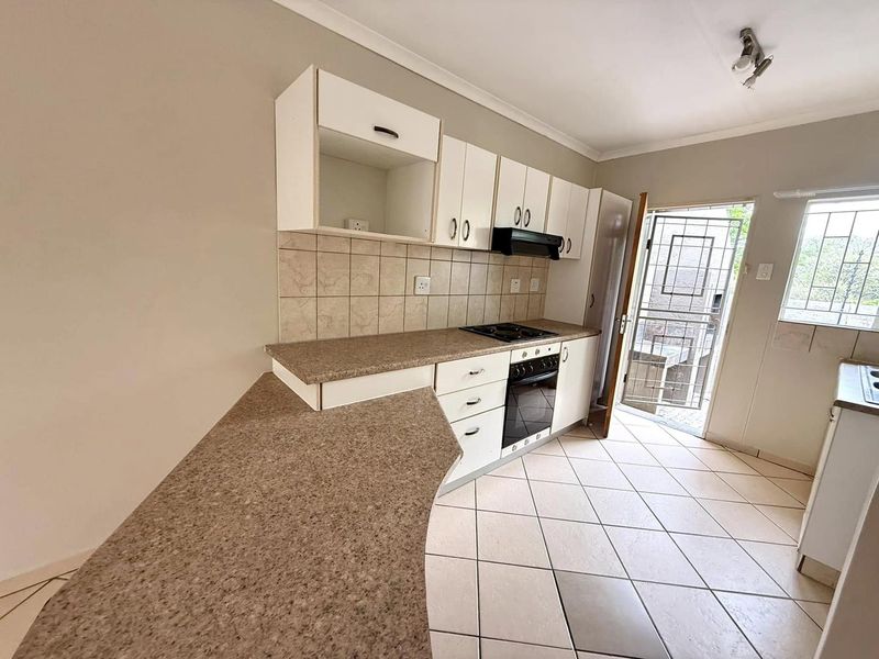 A functional kitchen featuring built-in cabinetry, laminate countertops, a built-in oven with hob, and direct access to an exterior security gate.