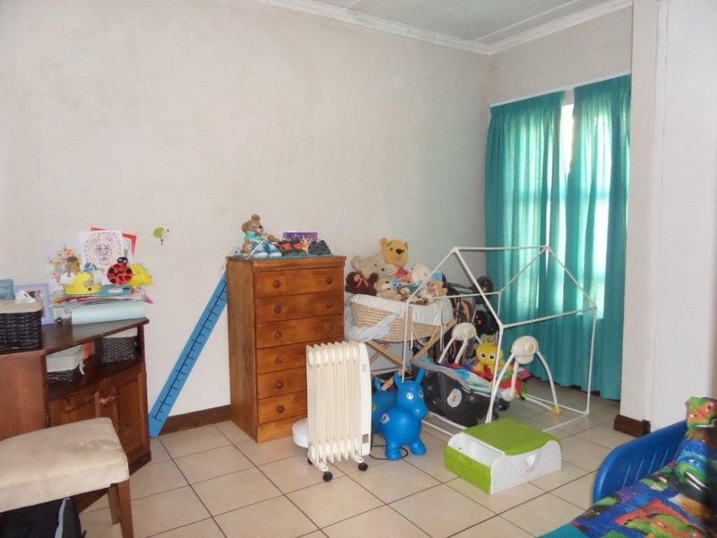 A bedroom featuring tiled flooring and a window with curtains, currently utilized as a nursery with visible wear on the wall finishes.