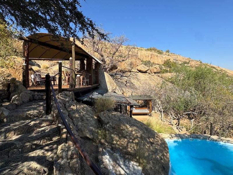 Outdoor lodge area featuring a swimming pool, stone staircase, and a covered patio nestled into a natural rocky landscape.