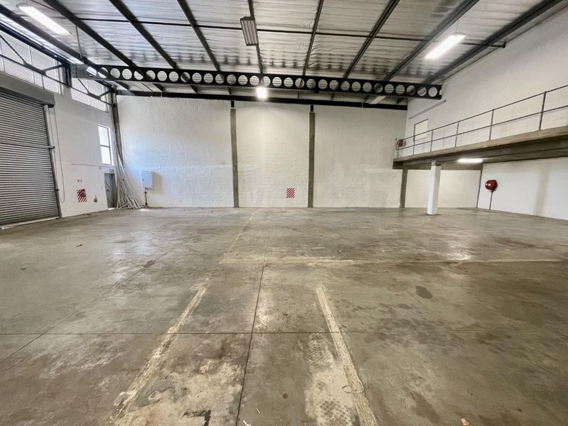 Spacious industrial warehouse unit featuring high ceilings, a mezzanine level, concrete flooring, and a large roller shutter door for easy access.