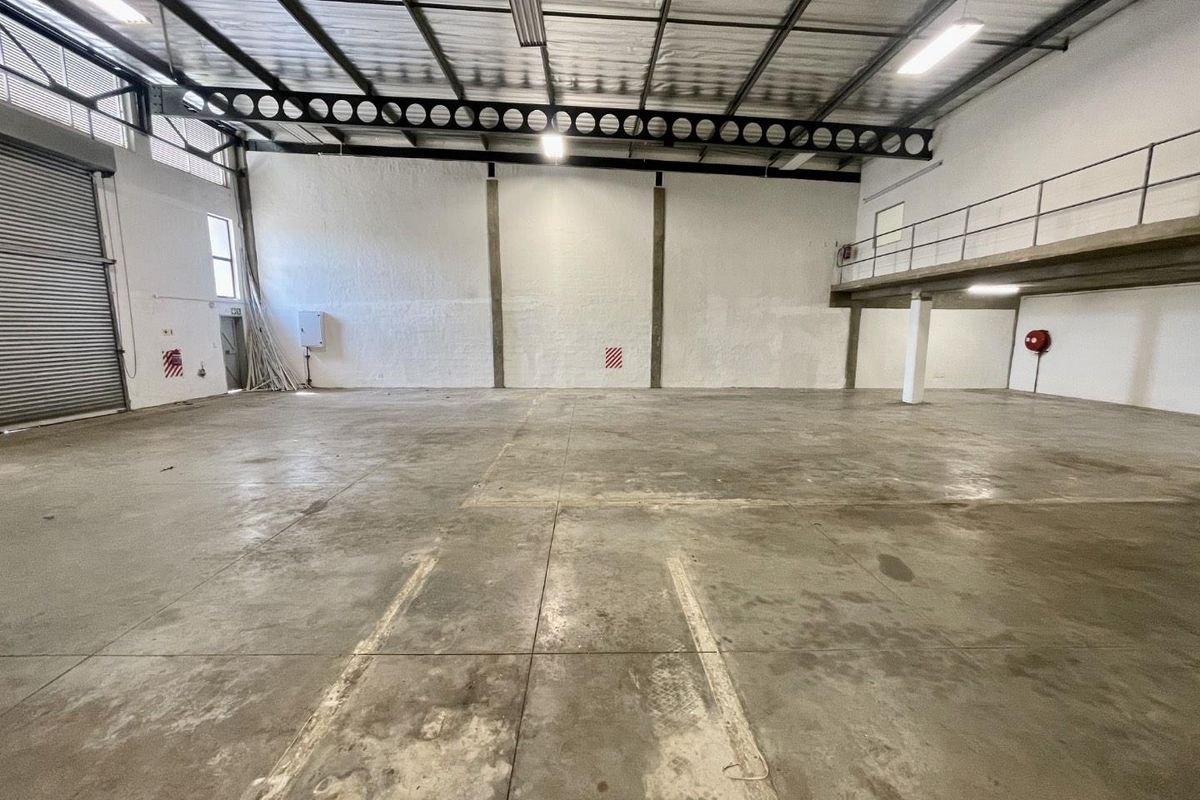 Spacious industrial warehouse unit featuring high ceilings, a mezzanine level, concrete flooring, and a large roller shutter door for easy access.