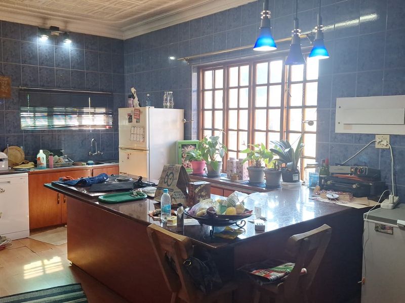 Spacious kitchen featuring a large central island, granite countertops, wooden cabinetry, and blue tiled walls, offering a functional layout with ample workspace.