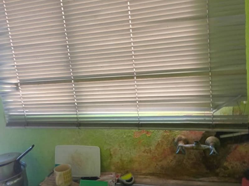 A kitchen sink area featuring a stainless steel basin and faucet, currently showing significant wall surface deterioration and peeling paint.