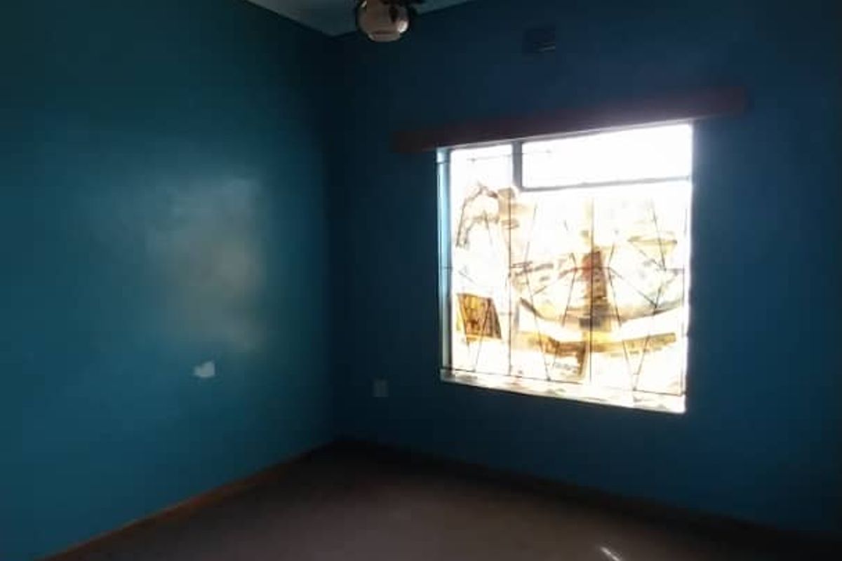 An empty bedroom featuring blue painted walls, carpet flooring, and a window fitted with security bars.