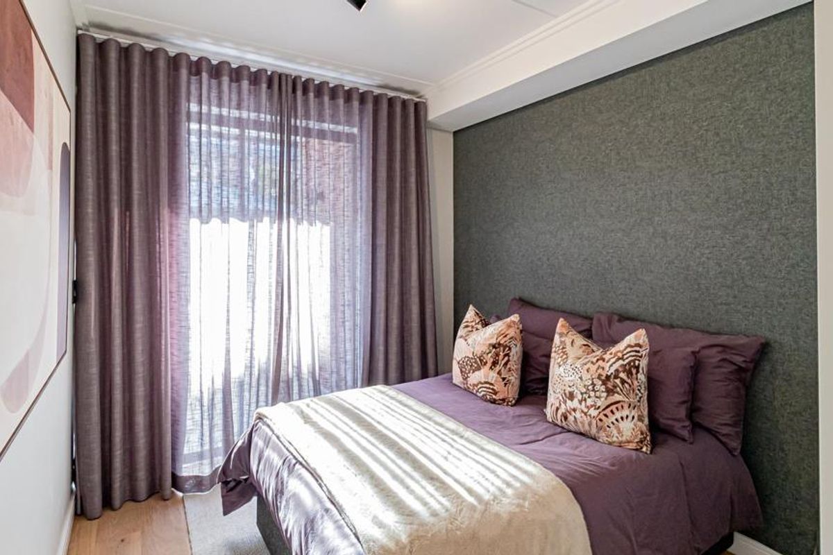 A well-presented bedroom featuring a textured accent wall, timber flooring, and floor-to-ceiling curtains providing natural light.