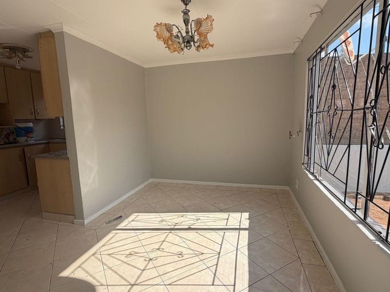 An open-plan living and kitchen area featuring tiled flooring, built-in cabinetry with stone countertops, and security bars on the windows.
