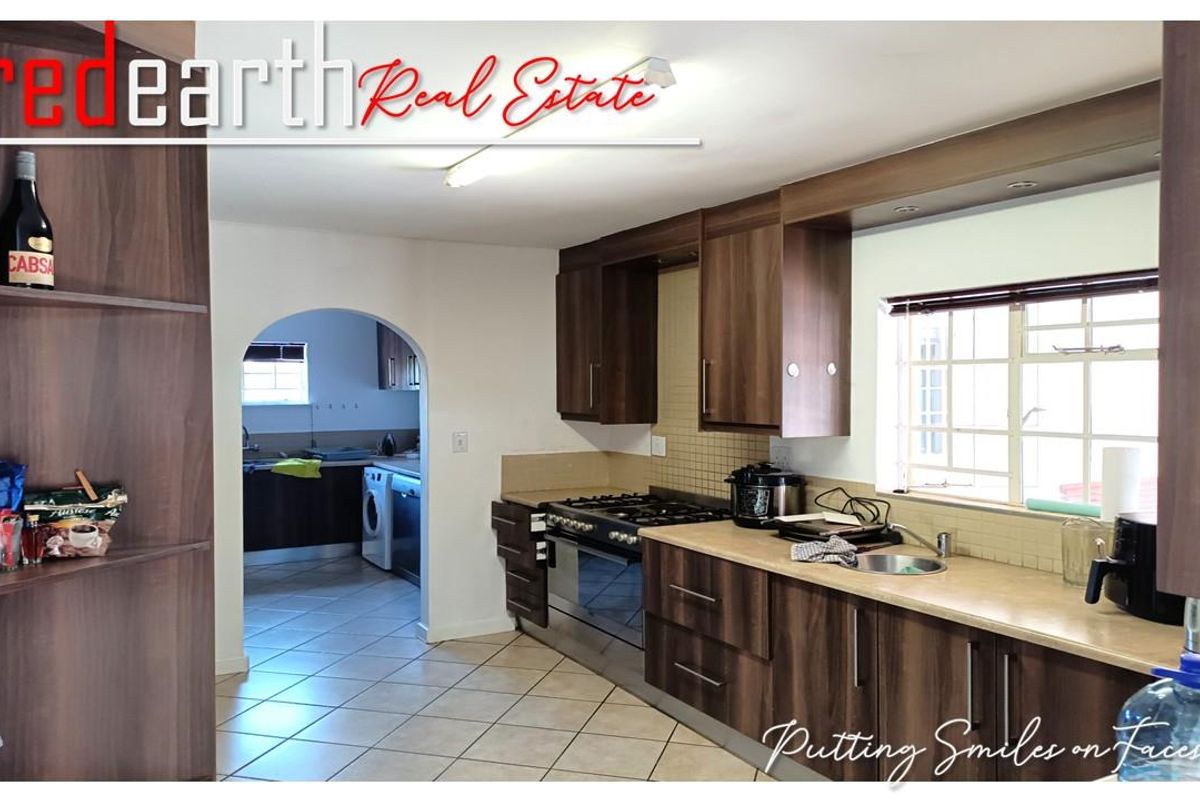 A functional kitchen featuring dark wood cabinetry, tiled flooring, a gas stove, and an arched doorway leading to a separate scullery area.