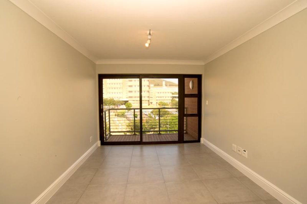 An empty, well-lit living area featuring neutral tiled flooring, cove cornicing, and a large sliding glass door providing access to a private balcony.