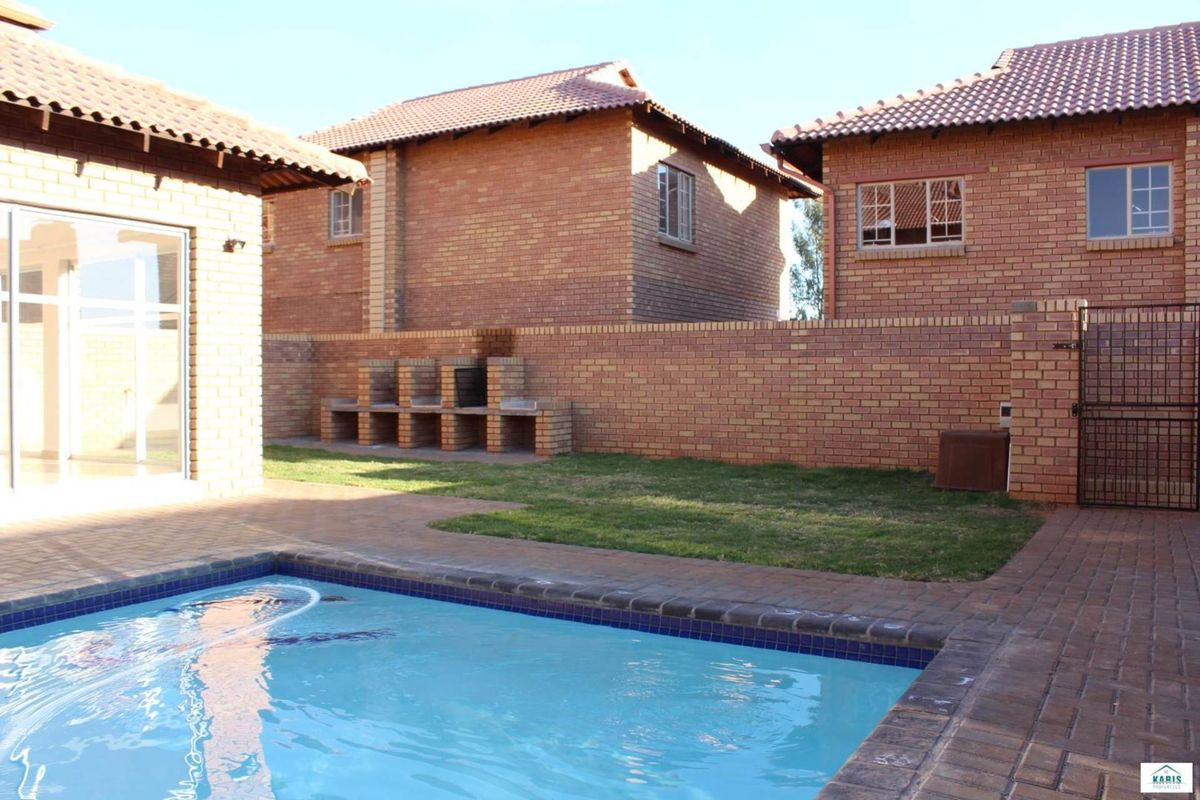 Rear exterior view featuring a swimming pool, paved patio, and a built-in brick braai area set against a private brick-walled garden.