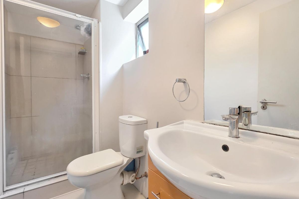 A functional bathroom featuring a shower enclosure, toilet, and vanity basin with a wall-mounted mirror and natural light from a casement window.