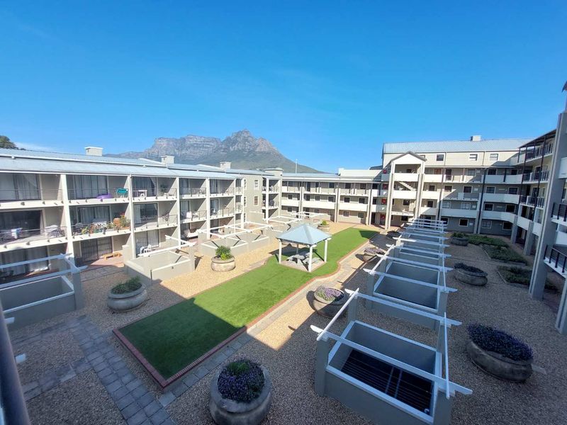 Elevated view of a well-maintained apartment complex courtyard featuring landscaped gardens, artificial lawn, a central gazebo, and private balconies.