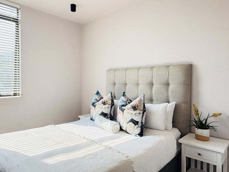 A bright and well-maintained bedroom featuring neutral walls, a window with venetian blinds, and a modern ceiling light fixture.