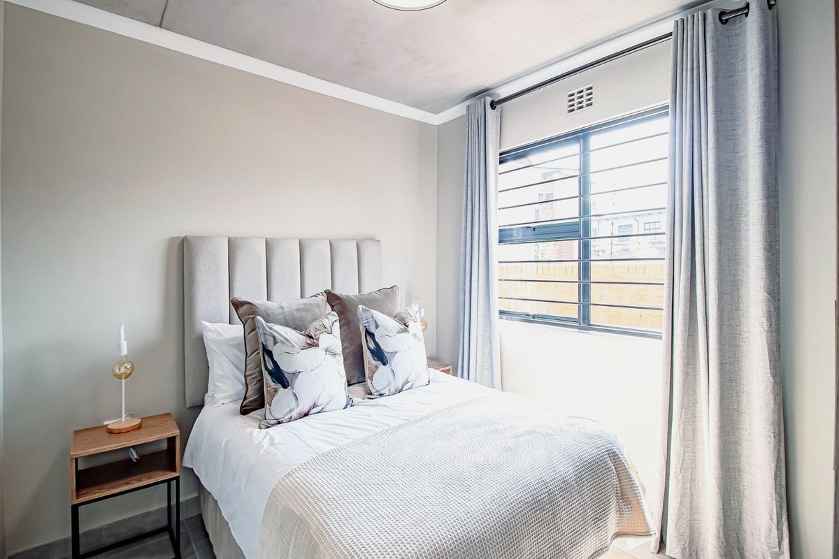 A well-maintained bedroom featuring neutral wall tones, a window with security bars, and classic cornice detailing.