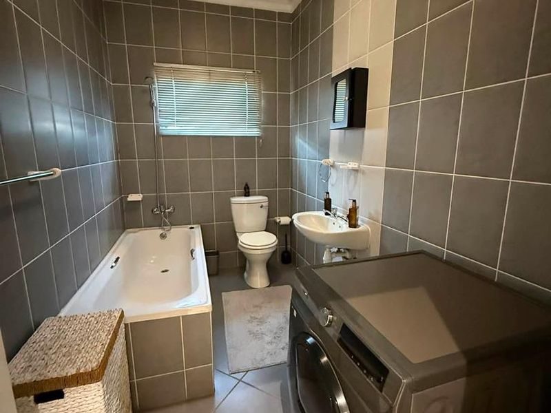 A functional bathroom featuring a bathtub, pedestal sink, toilet, and neutral grey wall and floor tiling.