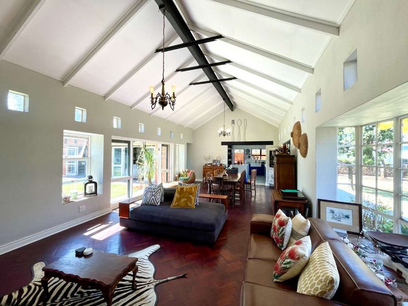 Spacious open-plan living and dining area featuring a dramatic vaulted ceiling with exposed steel trusses, herringbone parquet flooring, and abundant natural light.