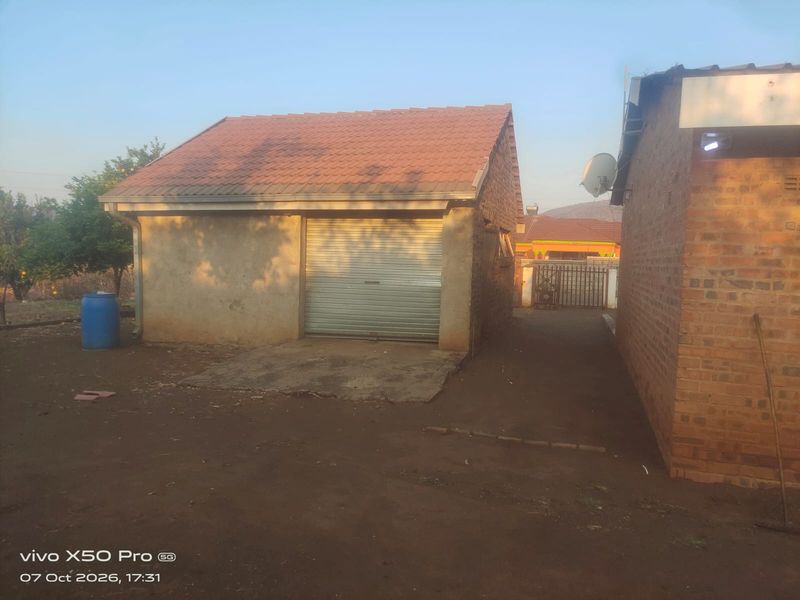 A detached garage with a roller shutter door and tiled roof, situated on an unpaved plot.