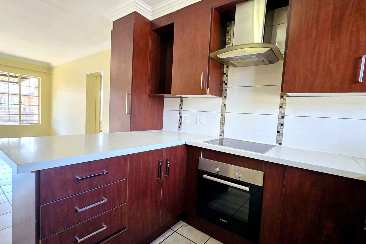 A functional kitchen featuring dark wood cabinetry, a built-in oven, extractor fan, and a breakfast bar counter, seamlessly flowing into the adjacent living area.