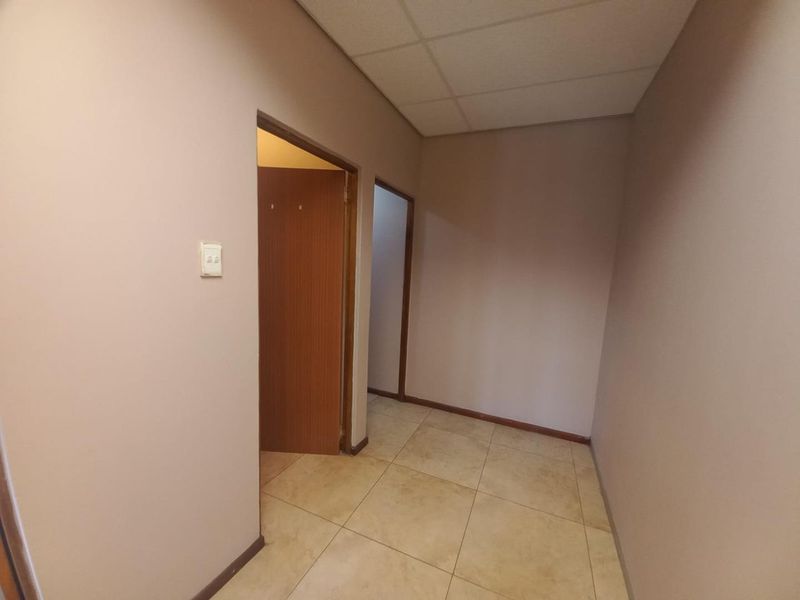 A vacant hallway featuring tiled flooring and a suspended ceiling, providing access to multiple internal rooms.