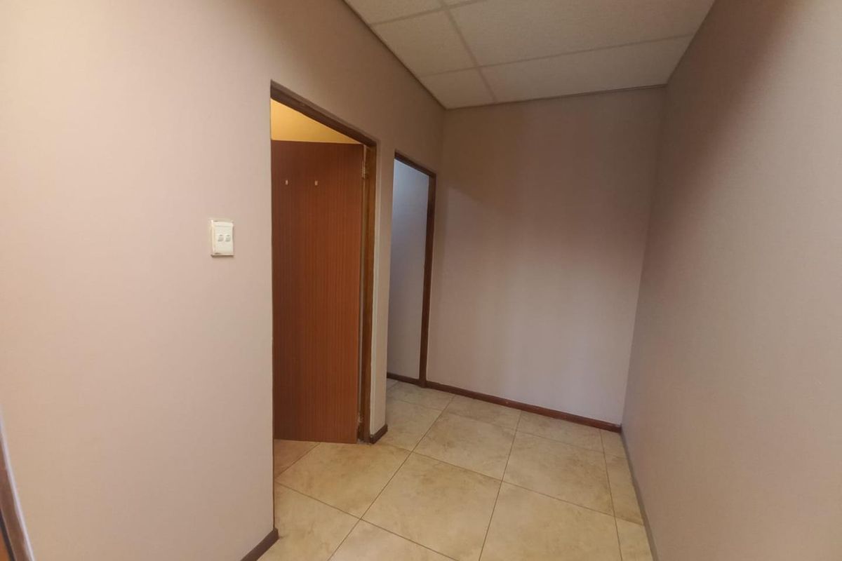 A vacant hallway featuring tiled flooring and a suspended ceiling, providing access to multiple internal rooms.