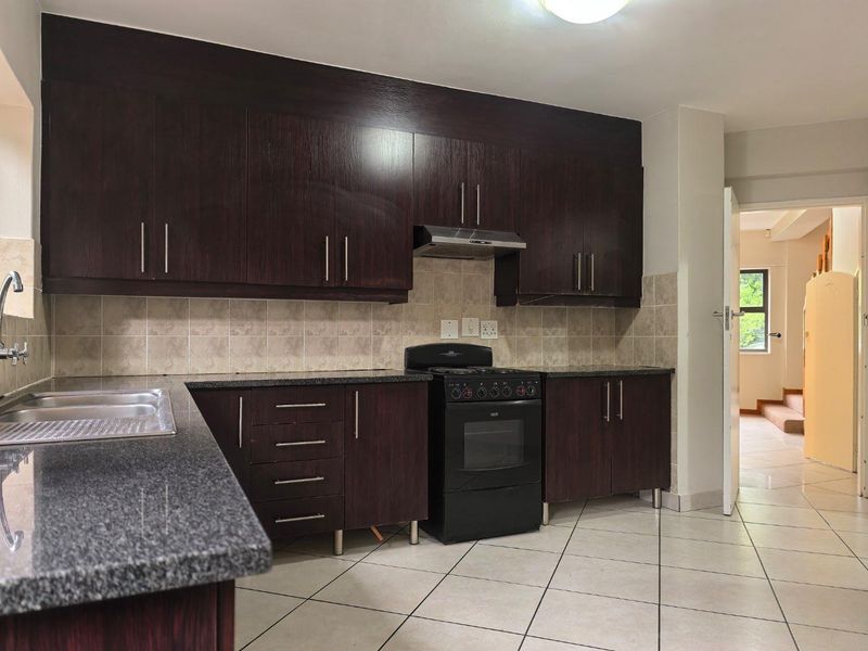 A functional kitchen featuring dark wood cabinetry, granite countertops, a stainless steel sink, and a freestanding stove with an extractor fan.