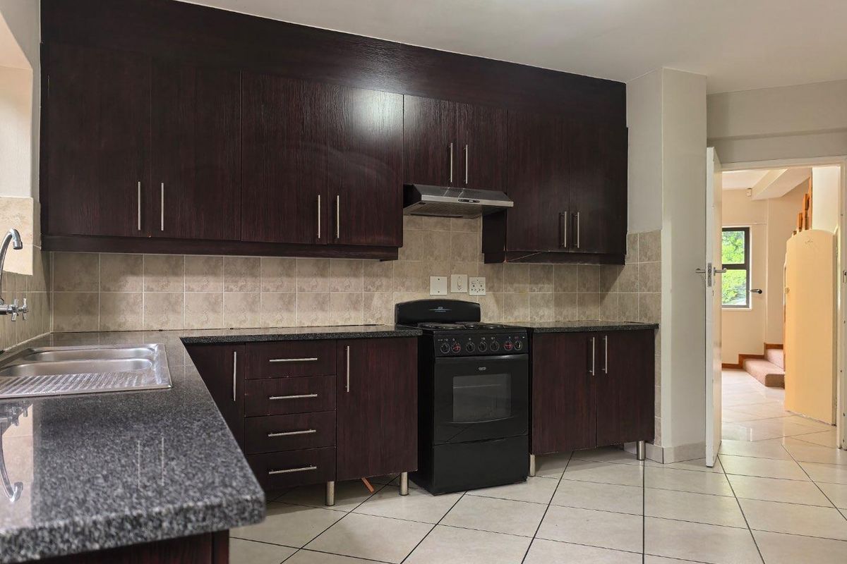 A functional kitchen featuring dark wood cabinetry, granite countertops, a stainless steel sink, and a freestanding stove with an extractor fan.
