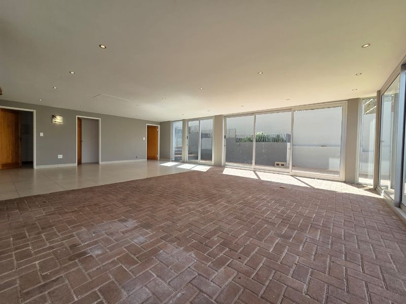 Spacious, empty living area featuring herringbone brick flooring, recessed downlights, and large sliding glass doors providing ample natural light and access to the exterior.