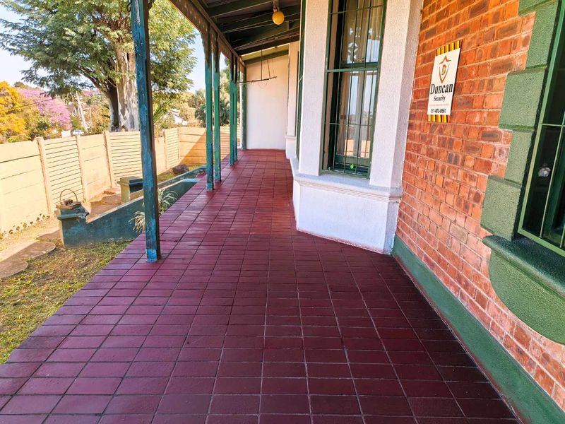 A covered veranda featuring red tiled flooring, brick exterior walls, and security-fitted windows, offering a classic outdoor transition space.