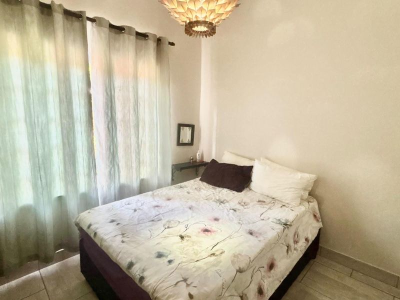 A bedroom featuring tiled flooring and a central ceiling light fixture, with natural light entering through a large window.