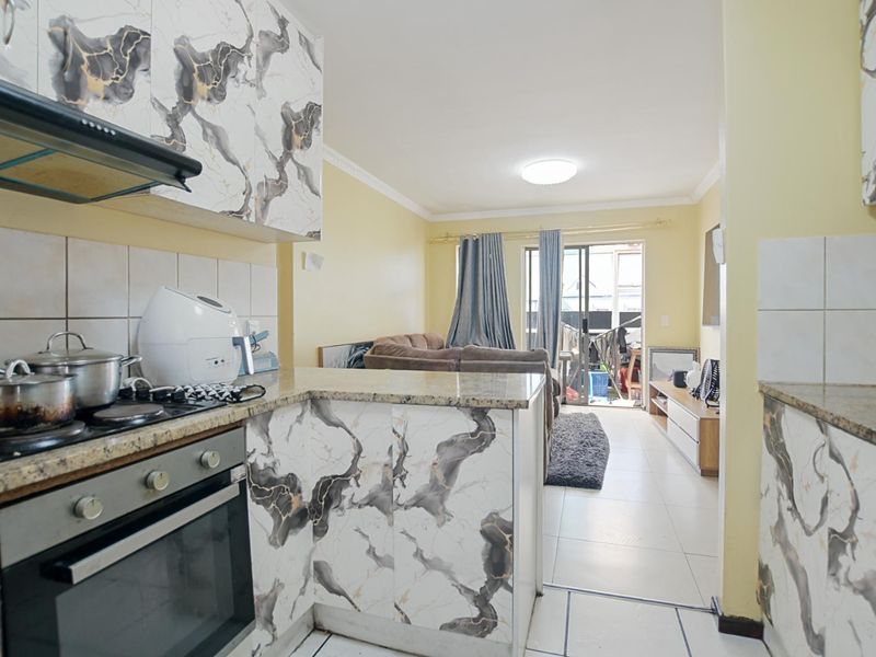 Open-plan kitchen and living area featuring marble-patterned cabinetry, granite countertops, built-in appliances, and direct access to a balcony through sliding glass doors.