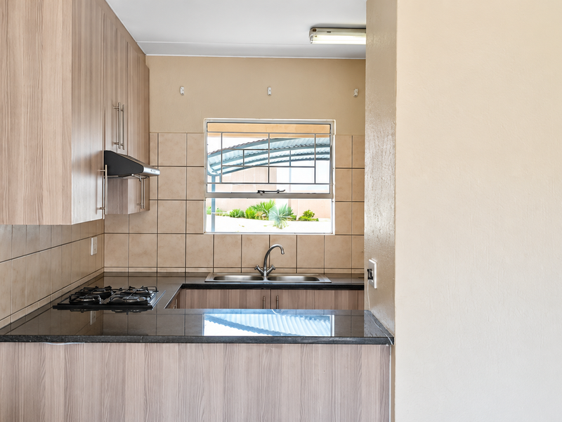 A functional kitchen featuring light wood-look cabinetry, dark granite countertops, a gas hob with extractor, and a tiled backsplash with a window view.