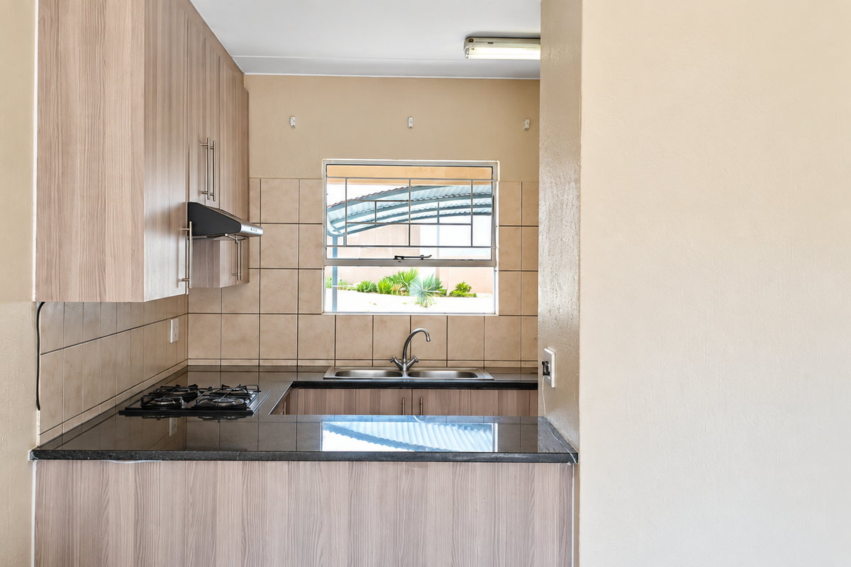 A functional kitchen featuring light wood-look cabinetry, dark granite countertops, a gas hob with extractor, and a tiled backsplash with a window view.