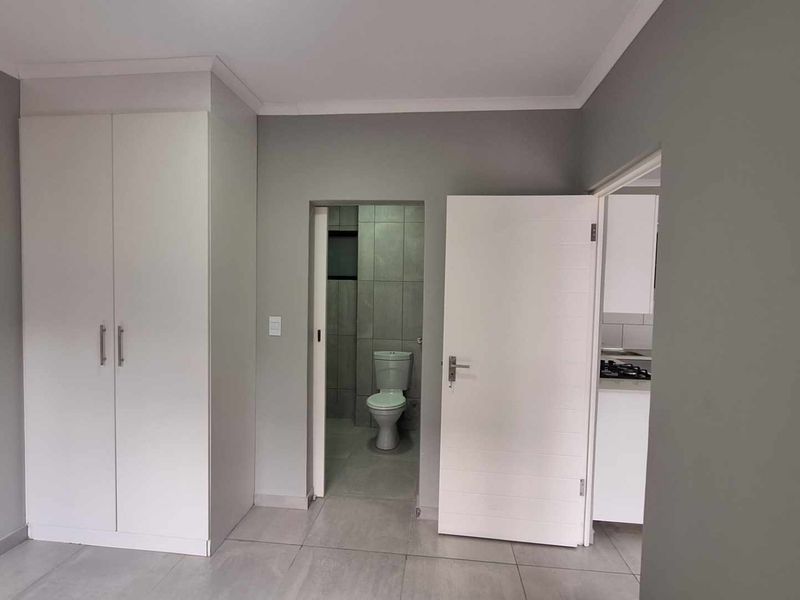 A clean, neutral-toned bedroom featuring tiled flooring, a built-in wardrobe, and direct access to an en-suite bathroom.