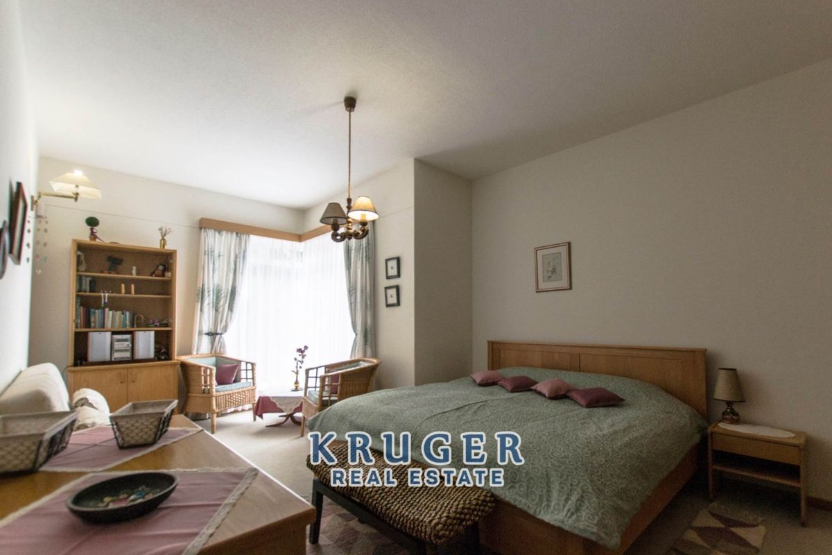 A spacious bedroom featuring neutral walls, carpeted flooring, and a large window with natural light.
