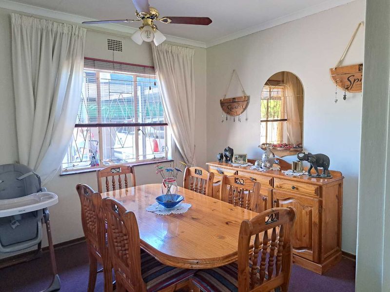 A functional dining room featuring a ceiling fan and a window fitted with security bars, providing a practical space for family meals.