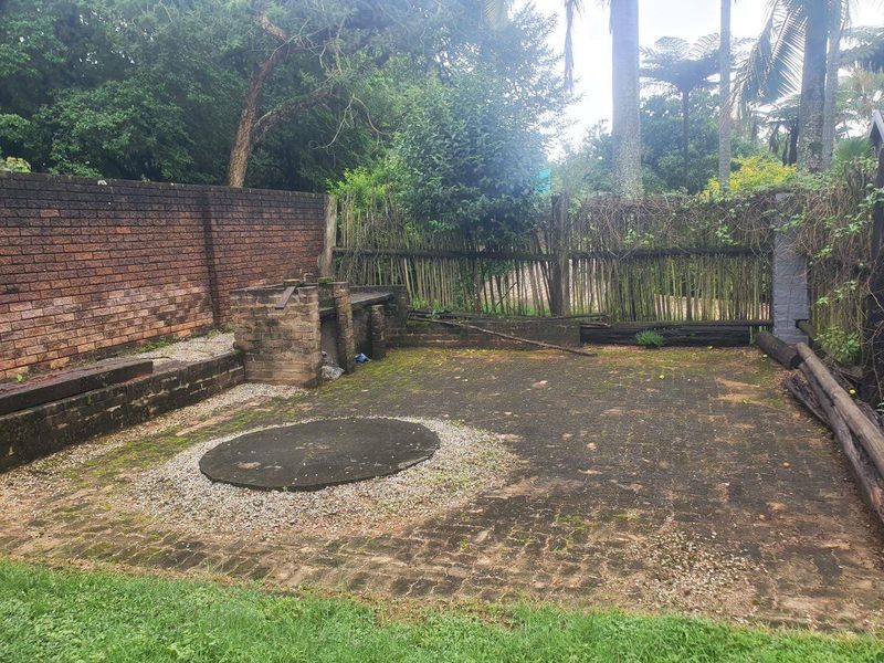 Outdoor patio area featuring a brick built-in braai, brick paving, and perimeter walling, requiring maintenance and landscaping to restore its functional appeal.
