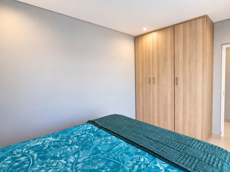 A well-maintained bedroom featuring neutral walls, modern tiled flooring, and floor-to-ceiling built-in wooden cupboards.