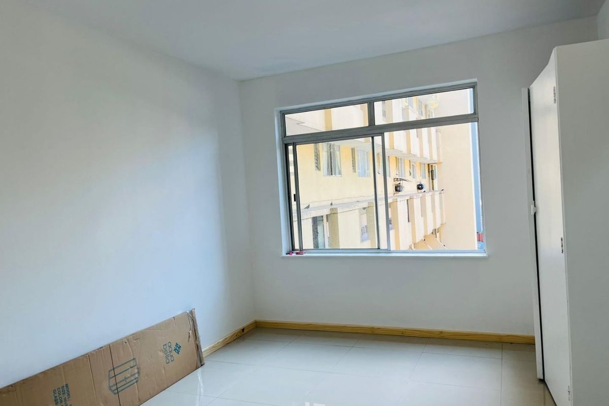 A bright, empty bedroom featuring tiled flooring, a sliding window, and a built-in wardrobe, ready for personalization.