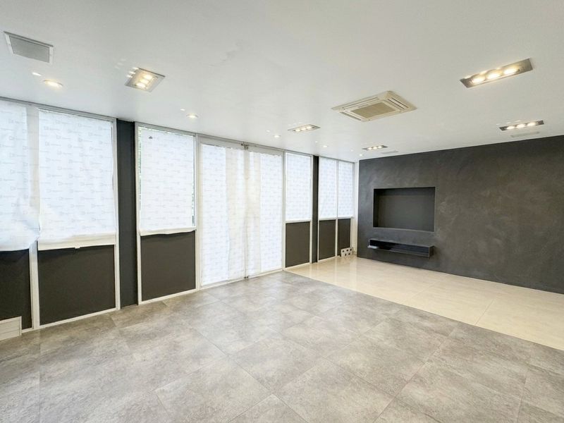 A spacious, modern living area featuring large windows, tiled flooring, recessed ceiling lights, and a built-in media wall niche with a dark feature finish.