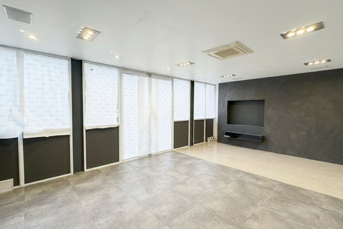 A spacious, modern living area featuring large windows, tiled flooring, recessed ceiling lights, and a built-in media wall niche with a dark feature finish.
