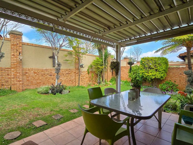 A covered outdoor patio area featuring tiled flooring and a metal roof, overlooking a private garden with a brick boundary wall.